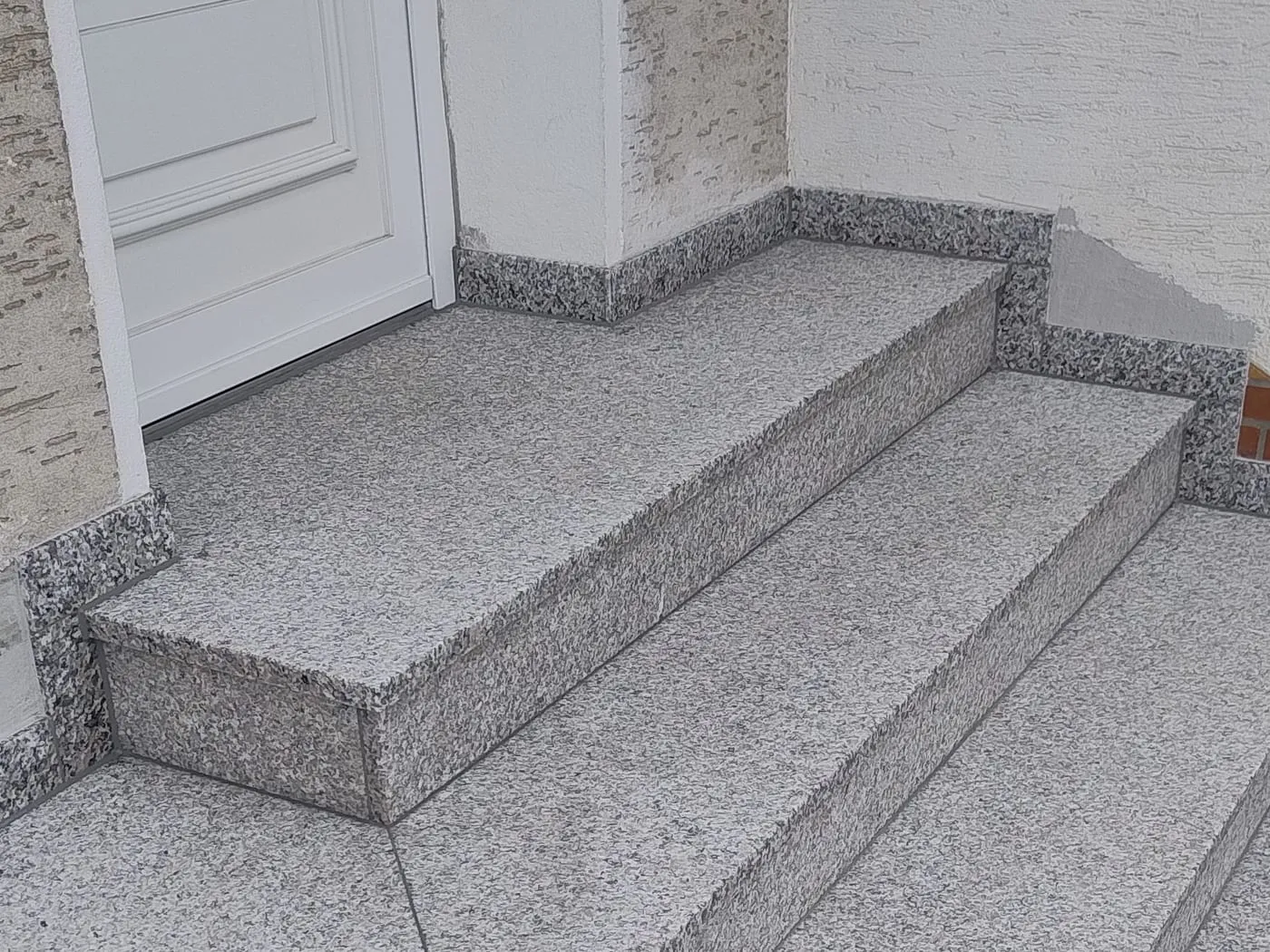 Eingangspodest und Stufen aus hellem gestocktem Granit vor einer weißen Haustür