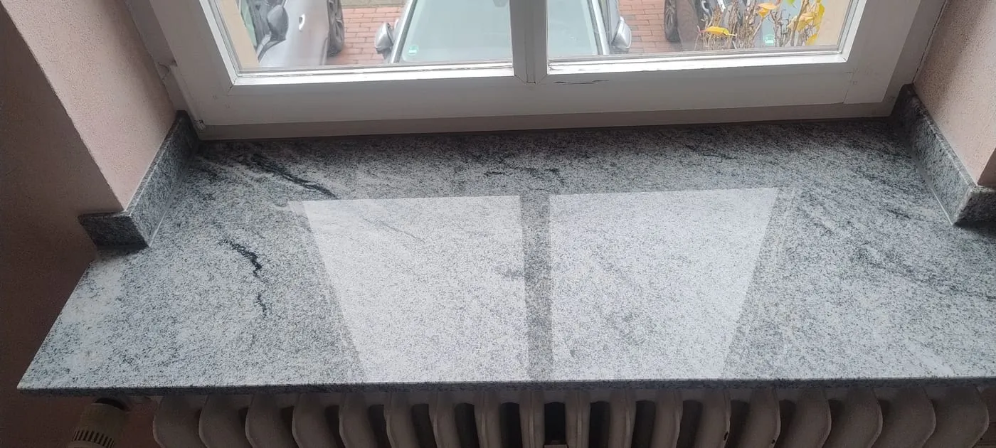 Neu eingebaute Fensterbank aus poliertem hellem Granit mit grauer Maserung, darunter der Heizkörper
