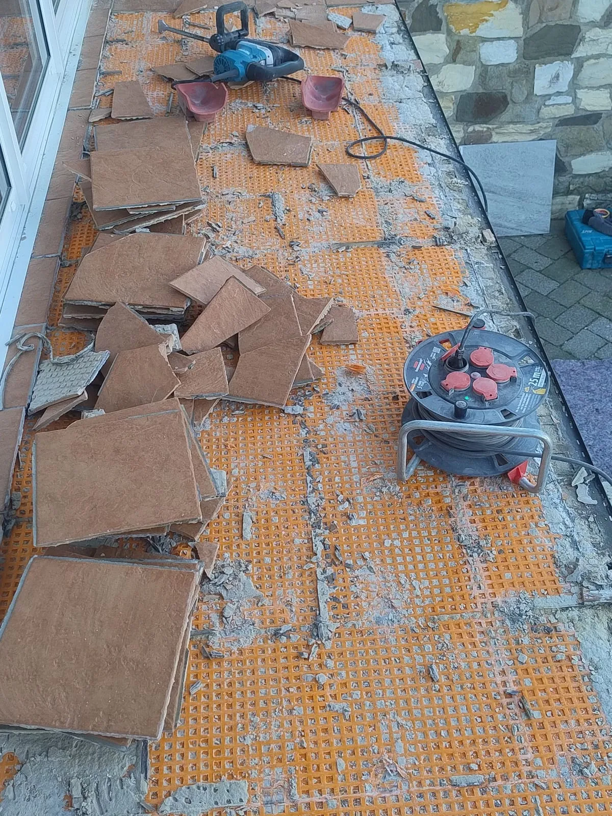 Rückbau der Terrasse: alte Fliesen abgetragen, darunter liegt die orangefarbene Entkopplungsmatte frei, Werkzeug steht bereit